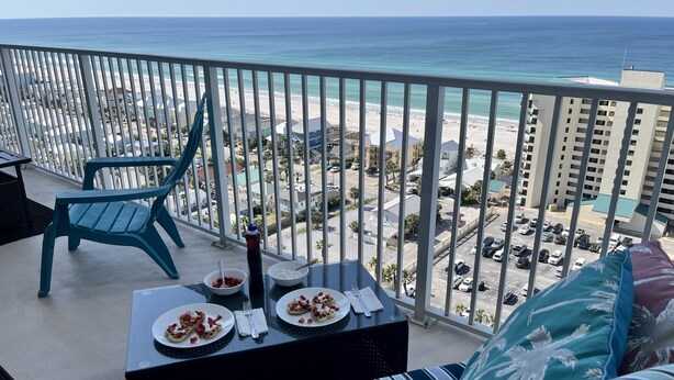 A balcony with a view of the beach and ocean, a dining table with plates of food, and a chair.