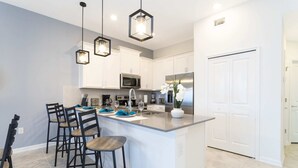 A modern kitchen with white cabinets, stainless steel appliances, and a central island with bar stools. - Unleash the Fun: 2BR Condo Sleeps 7 with Game Room (Four Corners)