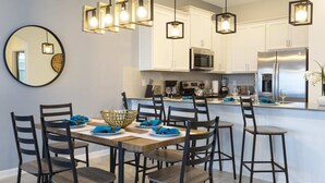 A modern kitchen with white cabinets, stainless steel appliances, and a wooden dining table with chairs. - Unleash the Fun: 2BR Condo Sleeps 7 with Game Room (Four Corners)