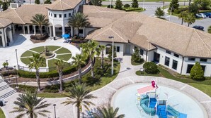An aerial view of a building with a circular courtyard, palm trees, and a water play area. - Unleash the Fun: 2BR Condo Sleeps 7 with Game Room (Four Corners)