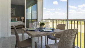 A balcony with wicker furniture, a table set with plates, glasses, and a pitcher, and a bed with a pillow and a lamp in the background. - Charming Villa | Themed Rooms | Prime Location (Four Corners)