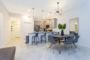 A modern kitchen with grey cabinets, a central island with bar stools, and a dining area with a wooden table and grey chairs.
