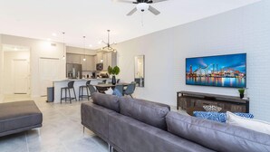 Un salon moderne avec un canapé gris, un coin repas avec une cuisine en arrière-plan et un ventilateur de plafond.