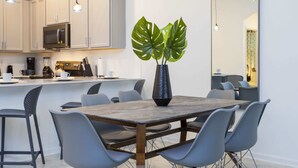 Une cuisine moderne avec des meubles blancs, un four à micro-ondes et une machine à café. On y trouve également un coin repas avec une table en bois et des chaises grises.