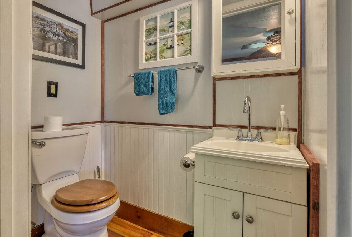 A bathroom with a wooden toilet, a white sink with a mirror, and a window with a view of a lighthouse.