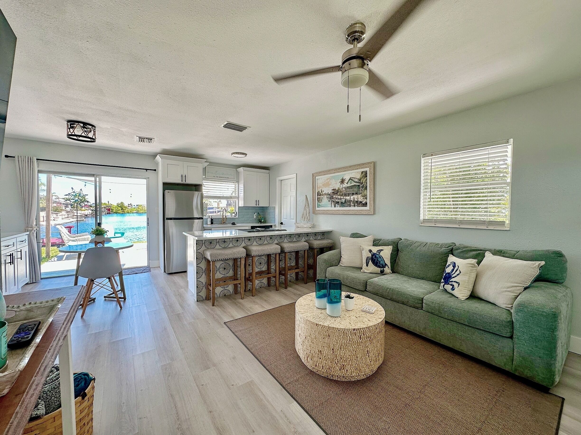 A spacious living area with a green sofa, a round coffee table, and a view of a pool through large windows.