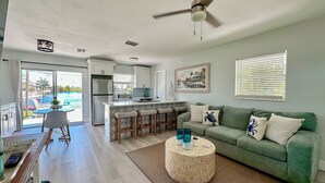 A spacious living area with a green sofa, a round coffee table, and a view of a pool through large windows.