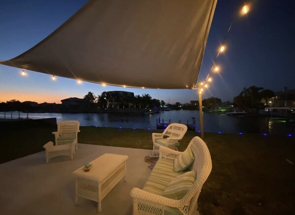 Relax by the serene water's edge in this tranquil seating area, complete with a shaded canopy and comfortable wicker furniture.