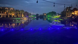 A nighttime view of a waterfront area with a boat docked near the shore, illuminated by blue and green lights.