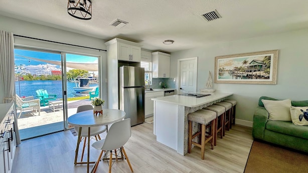 A modern kitchen with a large island, a dining area with chairs, a green sofa, and a view of a pool and water body.