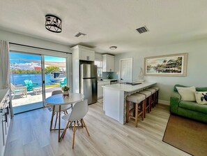 A modern kitchen with a large island, a dining area with chairs, a green sofa, and a view of a pool and water body.