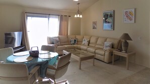 A living room with a sofa, coffee table, TV, and a ceiling fan. - Palm Desert retreat right on the golf course with King en-suite  (Palm Desert)