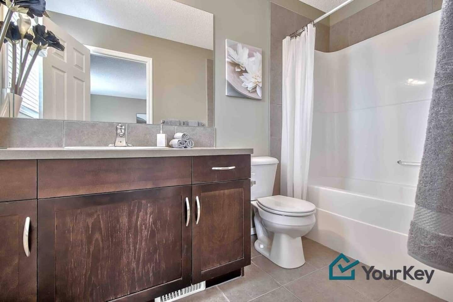 A modern bathroom with a dark wood vanity, white toilet, and a shower area.