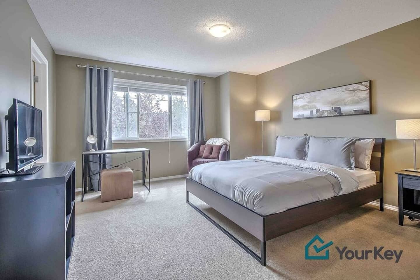 A modern hotel room with a large bed, a desk, a television, and a window with curtains.