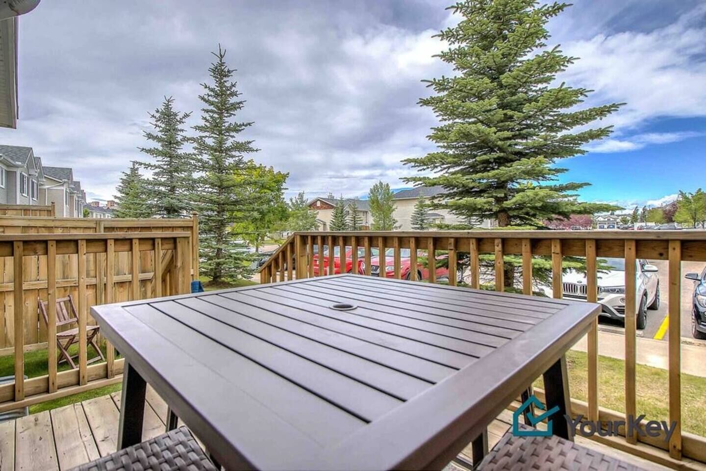 Une terrasse en bois avec une table et des chaises, entourée d’une clôture en bois et d’arbres.