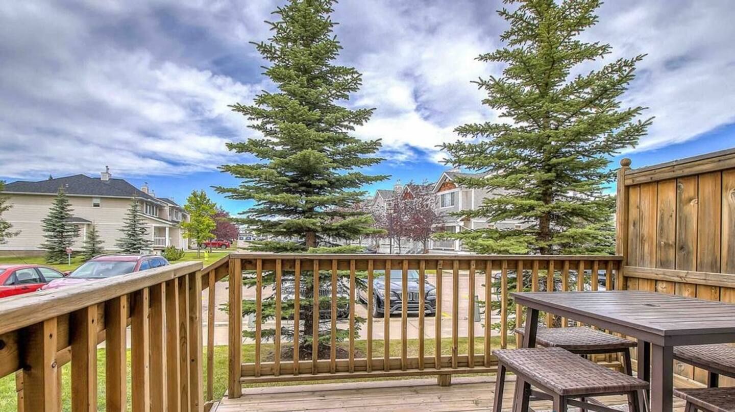 A wooden deck with a table and chairs, surrounded by tall trees and residential buildings.