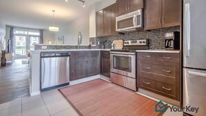 A modern kitchen with stainless steel appliances, dark wood cabinets, and a large island. - Enchanted Escape in Northwest Calgary Townhome (Calgary)