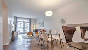 A modern dining area with a glass table, white chairs, and a hanging light fixture. - Enchanted Escape in Northwest Calgary Townhome (Calgary)