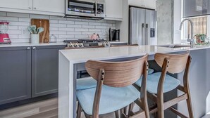 A modern kitchen with white cabinets, a built-in oven, a refrigerator, and a central island with bar stools.