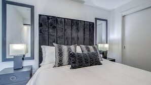 A modern bedroom with a large bed, two bedside tables, and a dark headboard. - Upscale Industrial Condo with Patio near LRT (Calgary)