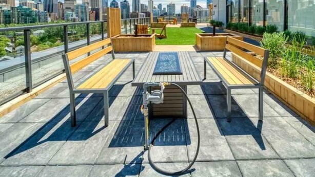 A rooftop terrace with wooden benches, a water feature, and a city skyline view. - Upscale Industrial Condo with Patio near LRT (Calgary)