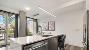 A modern kitchen with a large island, stainless steel appliances, and a bar area with stools. - Upscale Industrial Condo with Patio near LRT (Calgary)