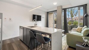 A modern kitchen with a central island, bar stools, and a flat-screen TV mounted on the wall. - Upscale Industrial Condo with Patio near LRT (Calgary)
