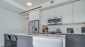 A modern kitchen with stainless steel appliances, a built-in island with bar stools, and a tiled backsplash. - Upscale Industrial Condo with Patio near LRT (Calgary)