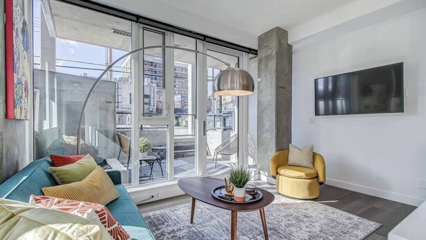 A modern living room with a sofa, a yellow armchair, a coffee table, and a large window with a view of the city.