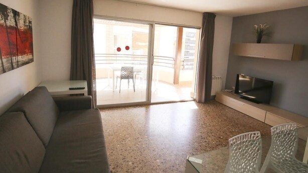 A living room with a sofa, a TV, a glass table with chairs, a balcony with a table and chairs, and a painting on the wall. - 101-LARESMAN-MAGNIFICENT AND SPACIOUS APARTMENT JUST 2 MINUTES FROM THE BEACH (SALOU)