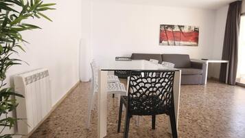 Un salon moderne avec une table en verre, des chaises blanches, un canapé gris et un tableau accroché au mur.