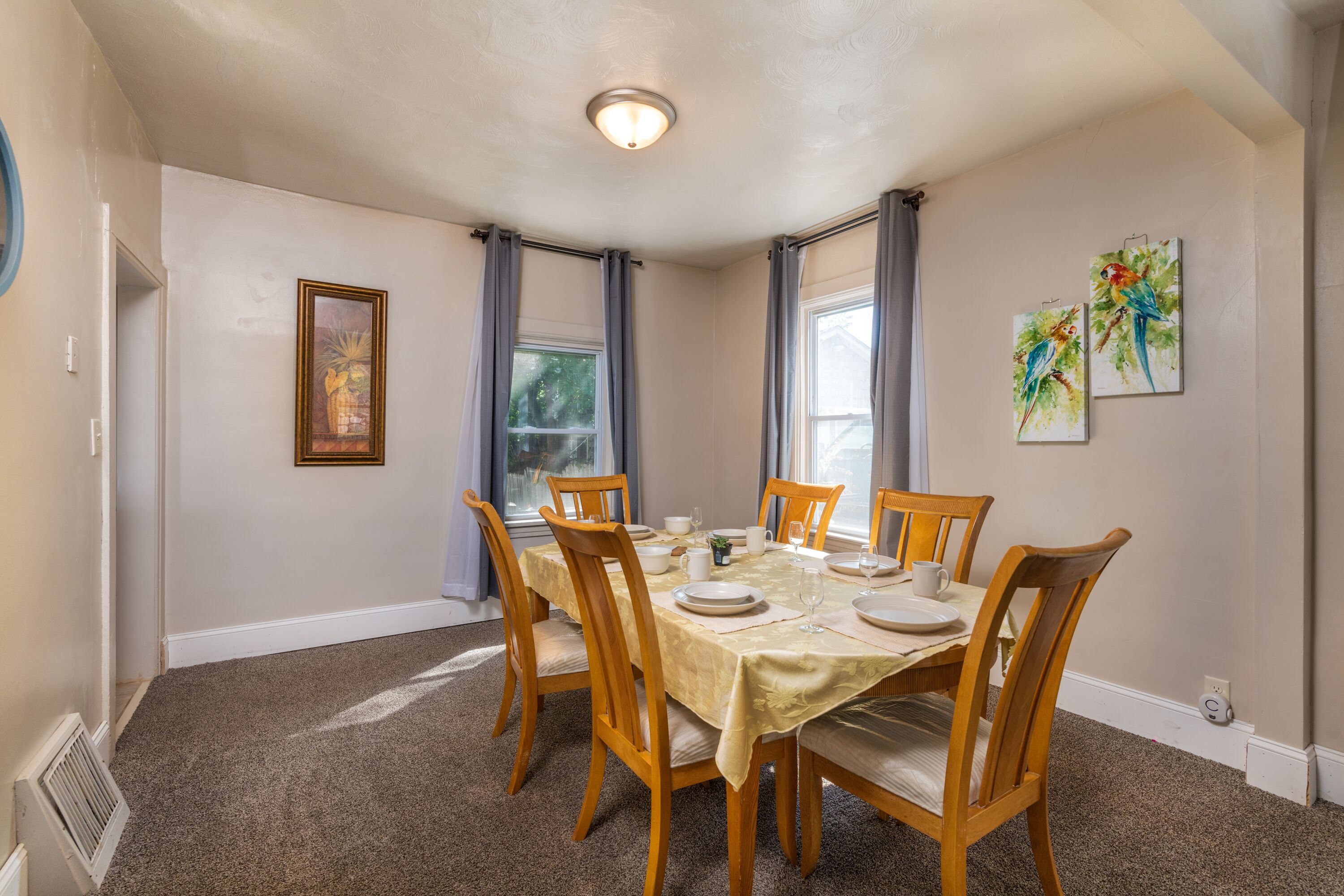 A dining room with a round table set for six, surrounded by wooden chairs with cushioned seats.