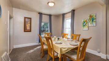 A dining room with a round table set for six, surrounded by wooden chairs with cushioned seats.