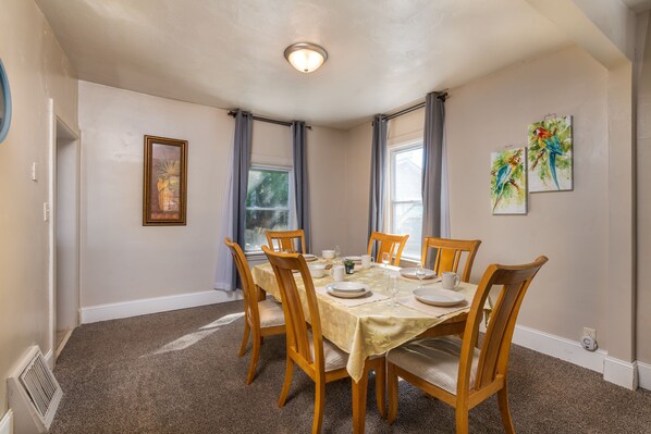 A dining room with a round table set for six, surrounded by wooden chairs with cushioned seats.