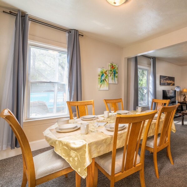 A dining area with a table set for six, wooden chairs, and a view of a swimming pool through the window.