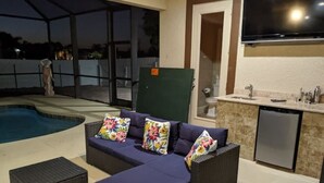 An outdoor seating area with a pool, a sofa with floral cushions, and a kitchen area with a dishwasher. - Cape Coral Paradise: Executive Home, weekly & monthly rates upon request. (Cape Coral)