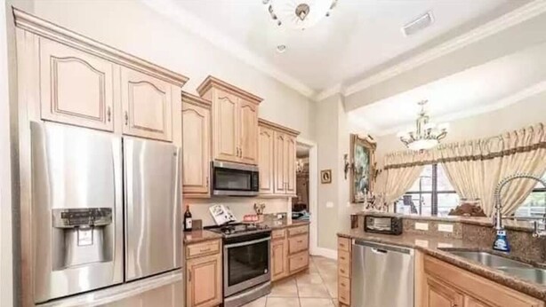 A spacious kitchen with stainless steel appliances, wooden cabinets, and a large window with curtains. - Cape Coral Paradise: Executive Home, weekly & monthly rates upon request. (Cape Coral)
