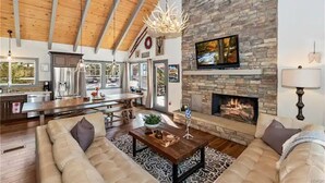 Un vaste espace de vie agrémenté d’une cheminée en pierre, de poutres apparentes en bois et d’un grand canapé.