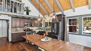 Une cuisine spacieuse avec des poutres en bois, des meubles de couleur sombre, des appareils électroménagers en acier inoxydable et un grand îlot central doté de sièges.