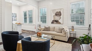 A spacious living room with a beige sofa, dark armchairs, and a glass coffee table. - 8B at Saint Philip Square, One Block to King, Spacious Group and Family Favorite (Charleston)