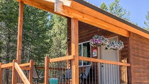 A wooden cabin with a covered deck, a staircase, and a hanging flower basket. - SUPER CUTE RUSTIC & CLEAN HOME 40 minutes to YNP (Island Park)