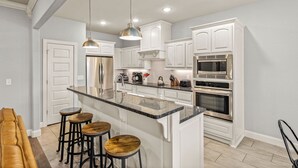 A modern kitchen with white cabinetry, stainless steel appliances, and a central island with stools.