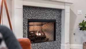 A fireplace with a mosaic tile surround, a white mantel, and a visible fire.