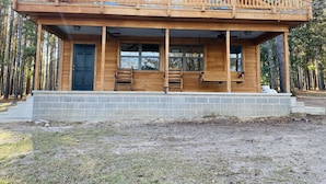 Une cabane en bois dotée d’un balcon, d’une porte d’entrée et d’un porche avec des bancs.