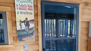 Une cabane en bois avec une pancarte indiquant «Bienvenue», une porte dotée d’un panneau en verre et un paillasson.