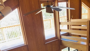 L’intérieur d’un chalet en bois est aménagé avec un lit en mezzanine, un canapé en cuir, un bureau et de grandes fenêtres qui offrent une vue sur l’extérieur.