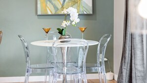 Un coin repas avec une table ronde, des chaises transparentes et un vase rempli de fleurs blanches.