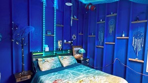 Habitació amb llit, una tauleta de nit, una làmpada i prestatges amb objectes decoratius.
