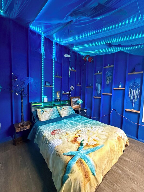 A room with a bed, a nightstand, a lamp, and shelves with decorative items.