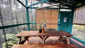 Taula de picnic de fusta amb una planta en test, en una habitació amb grans finestres i una porta verda.